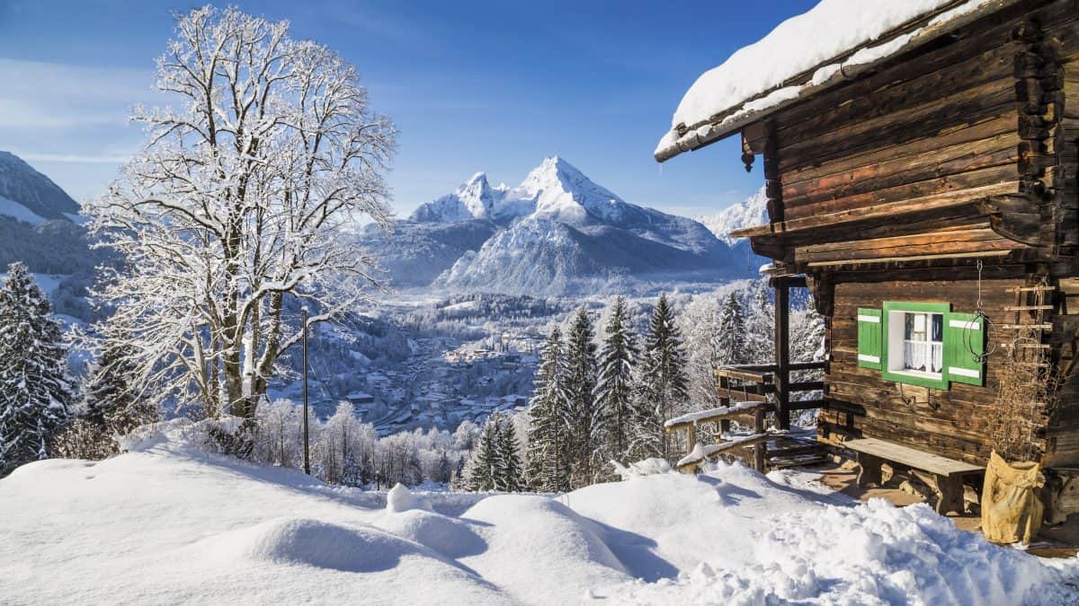 Uitzicht over besneeuwde bergen met bomen en een huisje
