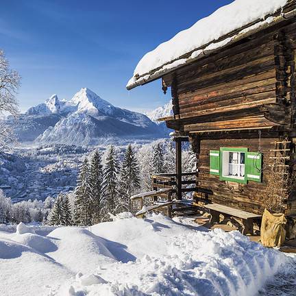 Uitzicht over besneeuwde bergen met bomen en een huisje