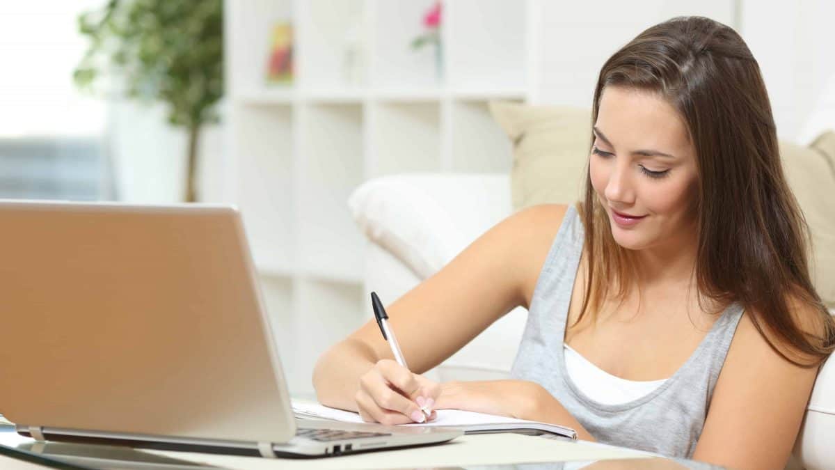 Vrouw schrijft op een notitieblok bij een laptop