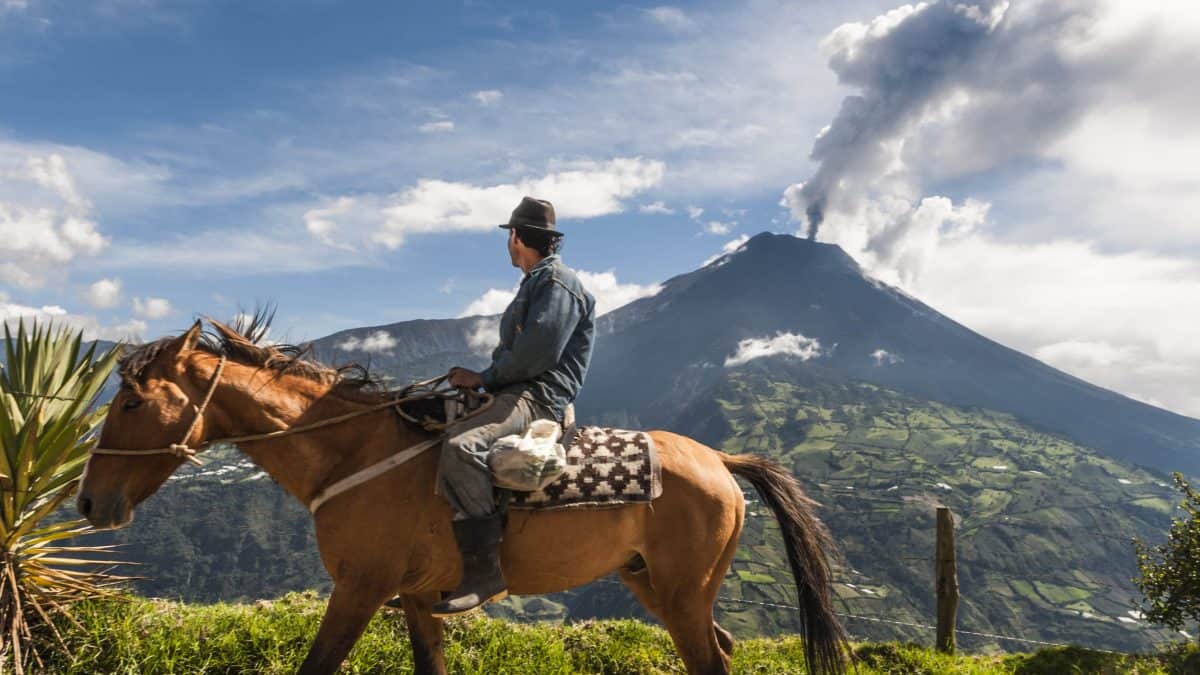 Man op paard met uitzicht op de Tungurahua vulkaan in Ecuador