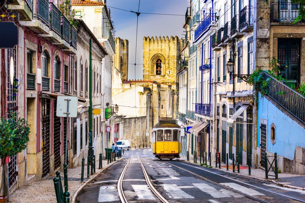 Tram tussen huizen met toren op de achtergrond in Lissabon, Portugal