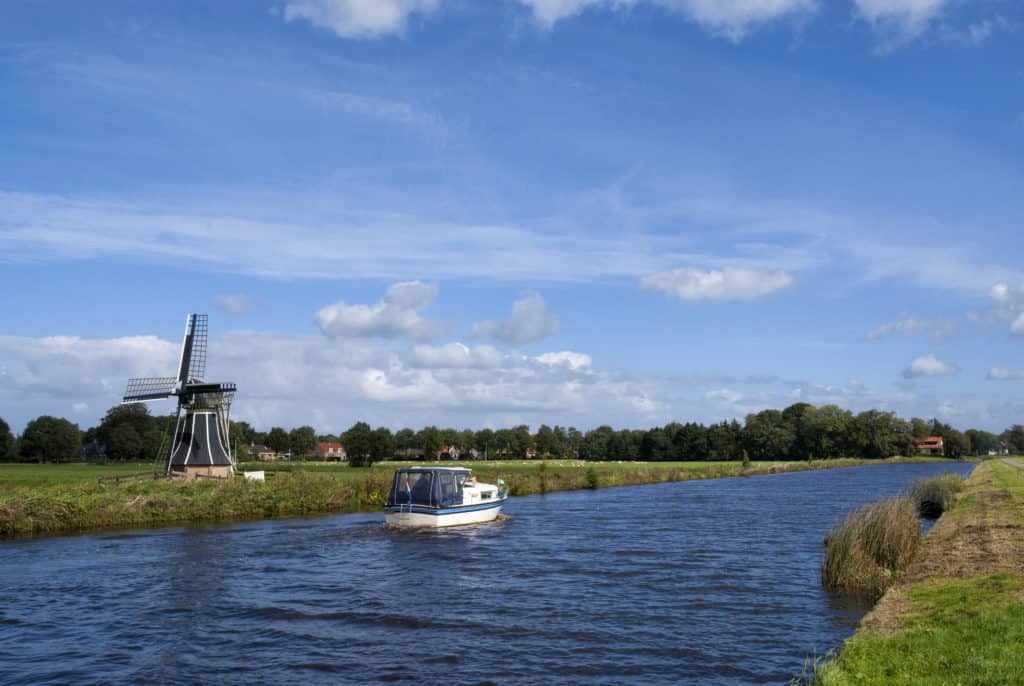 Boot in kanaal in Friesland met molen op de achtergrond