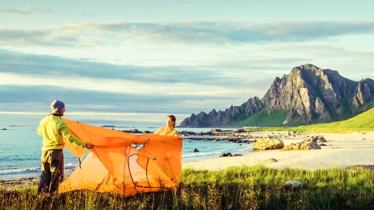 Man en vrouw zetten een tent op aan het strand en uitzicht op de bergen in Noorwegen