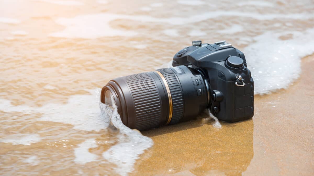 Spiegelreflexcamera wordt overspoeld door een kleine golf op het strand