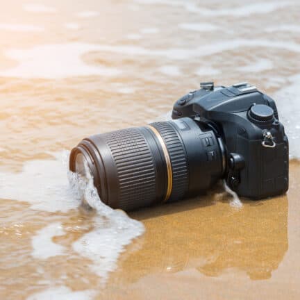 Spiegelreflexcamera wordt overspoeld door een kleine golf op het strand