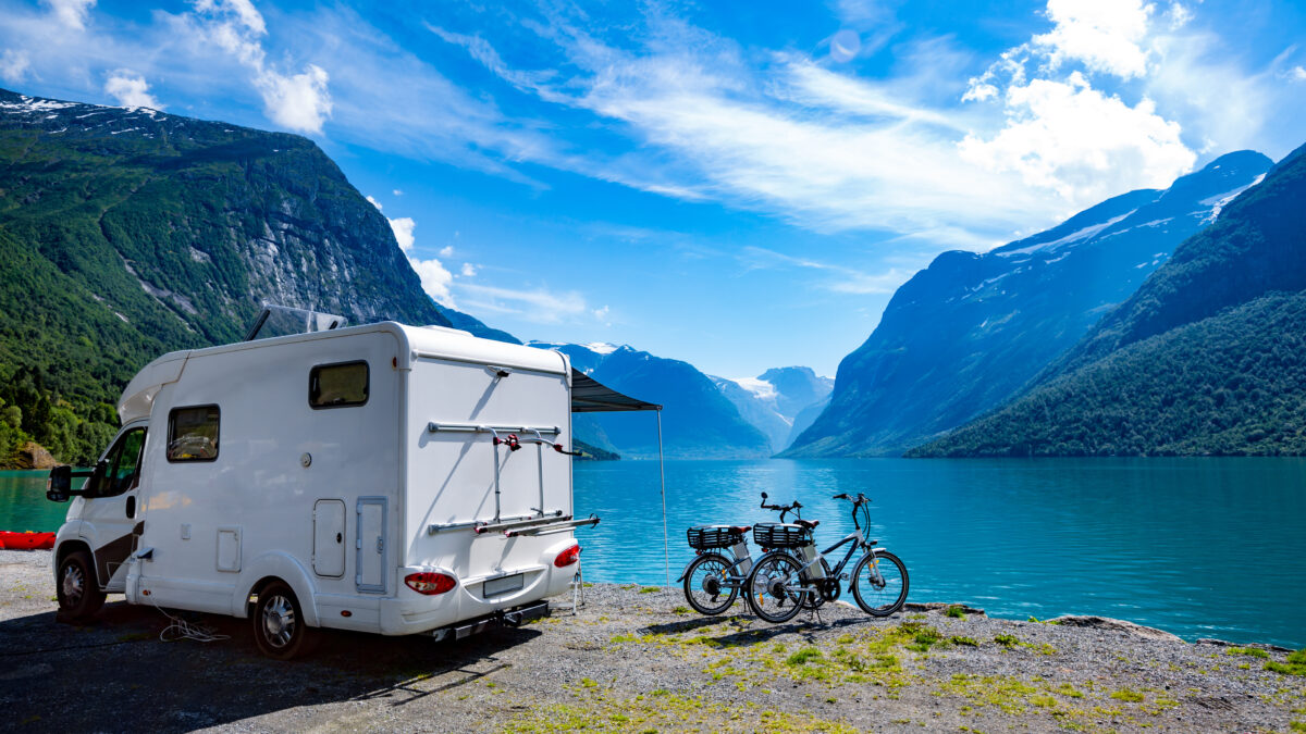 Witte camper met fietsen aan een meer en bergen in de verte