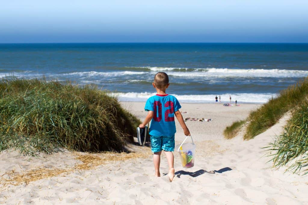 Kleine jongen loopt met strandspullen door de duinen richting het strand