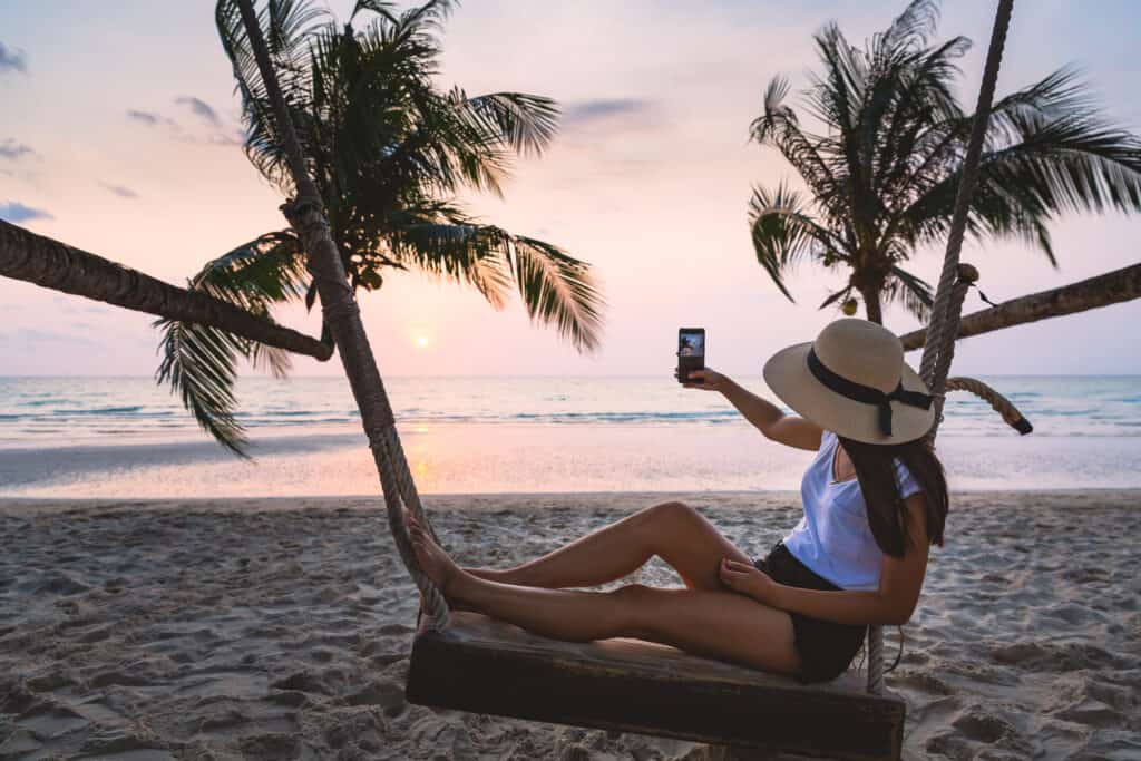 Vrouw in schommel op het strand maakt foto van de zonsondergang