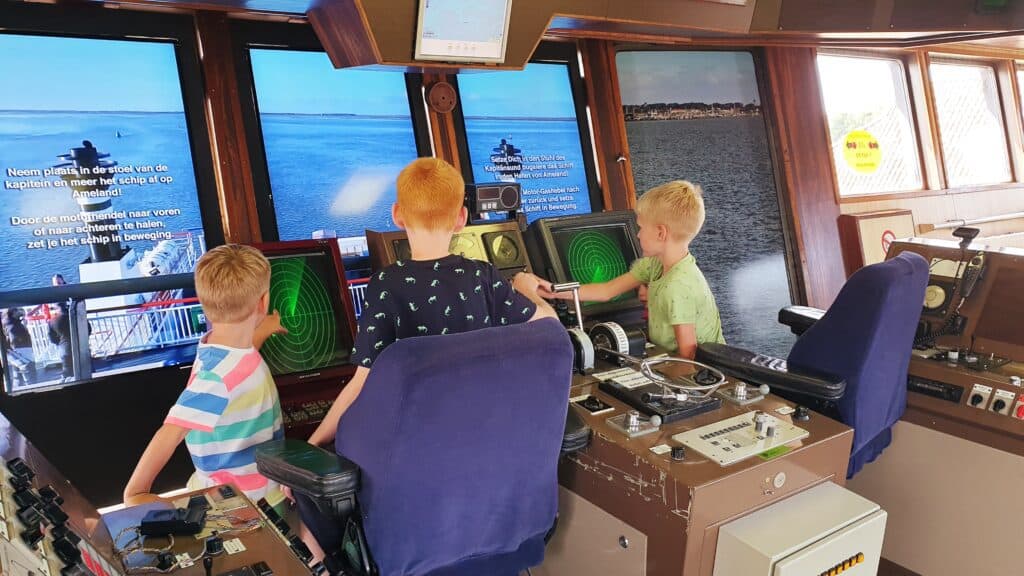 Drie kinderen aan het spelen op een simulator van een veerboot in het Abraham Fock museum